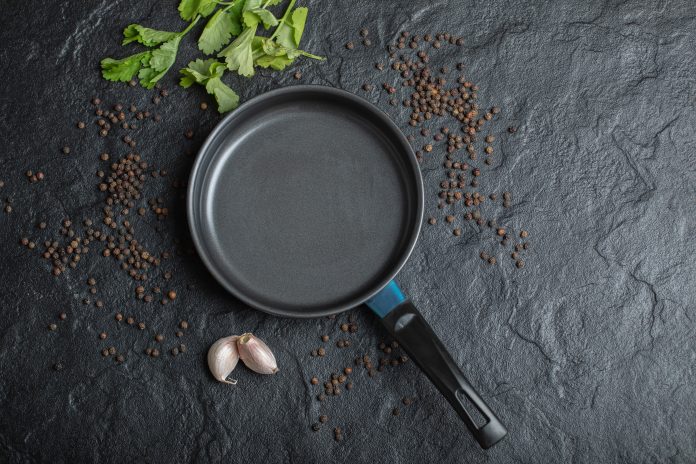 Top view of empty frying pan over black background with garlic and peppers
