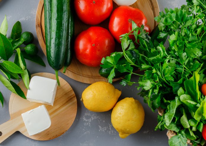 Top view tomatoes in cutting board with lemon, cucumber, cheese, greens on gray background. horizontal