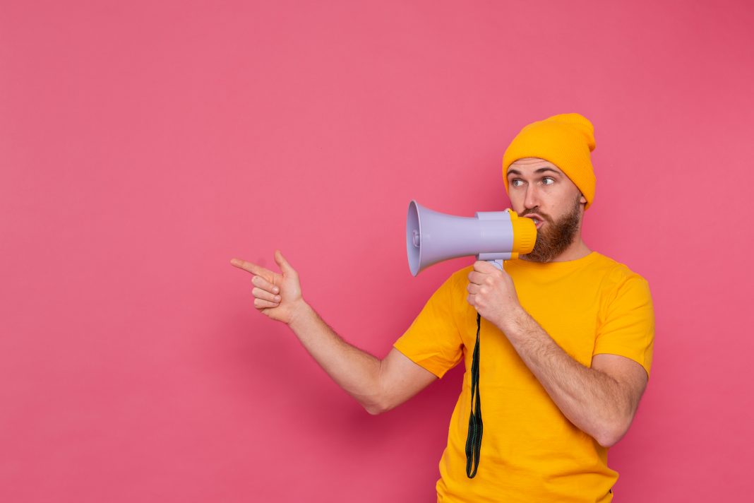 Attention! European man with megaphone pointing finger to the left on pink background