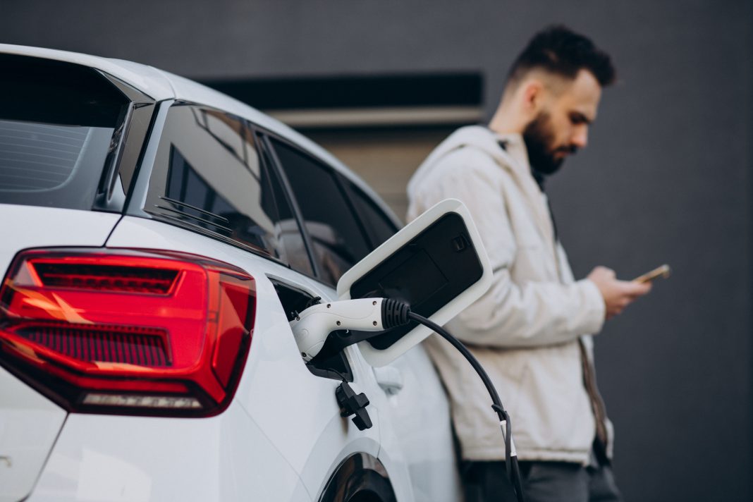 Man charging electric car by the house