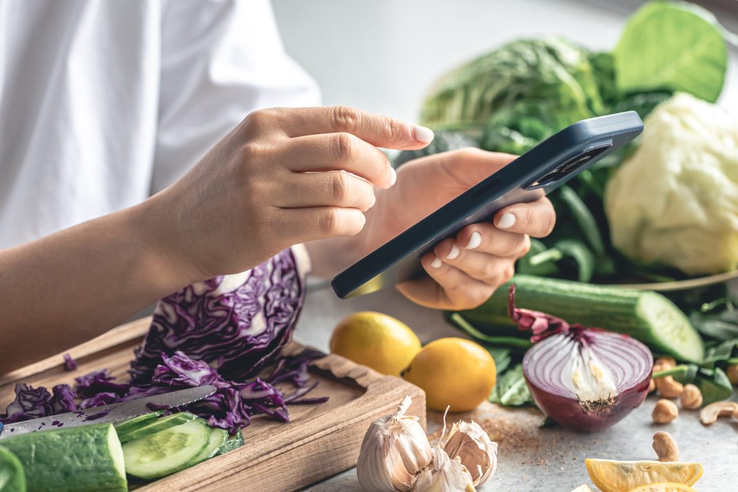 woman-uses-smartphone-kitchen-while-preparing-vegetable-salad